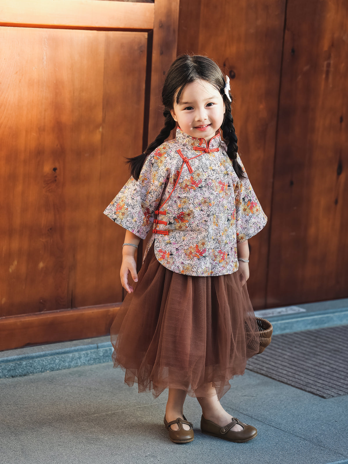 Girl wearing the floral Mandarin top and chestnut tulle skirt set by a wooden door