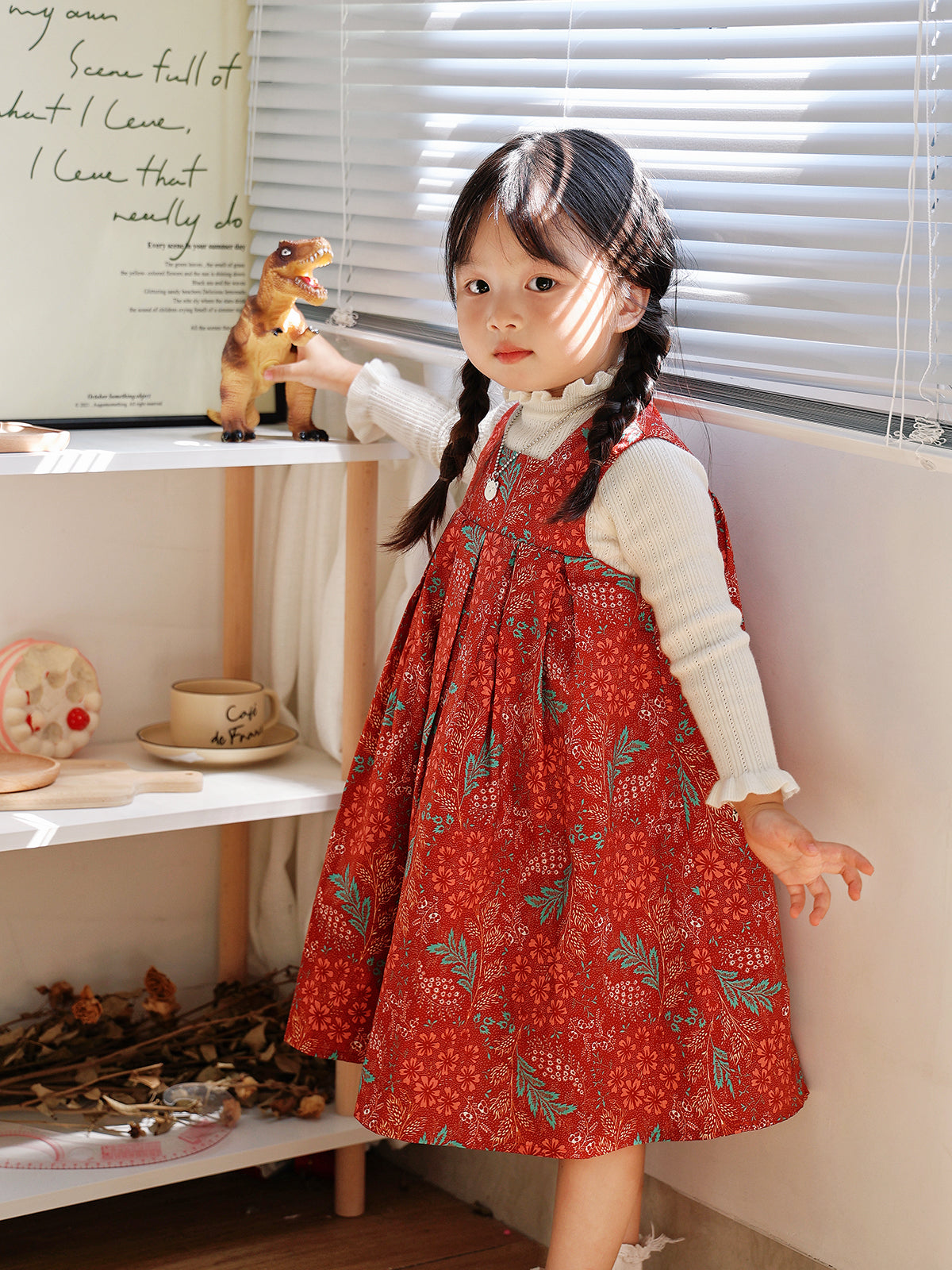 Girl wearing Holiday Bloom red floral dress layered over a white knit indoors