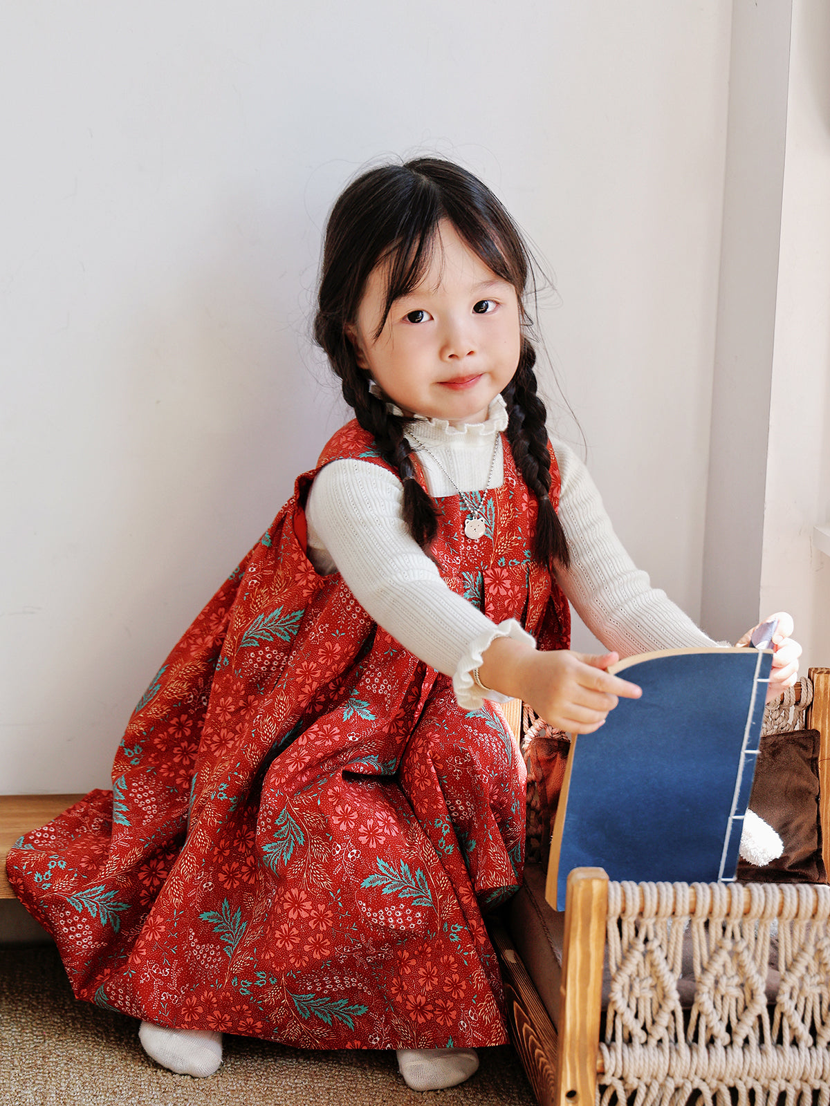 Girl seated wearing Holiday Bloom red floral dress with white knit layer