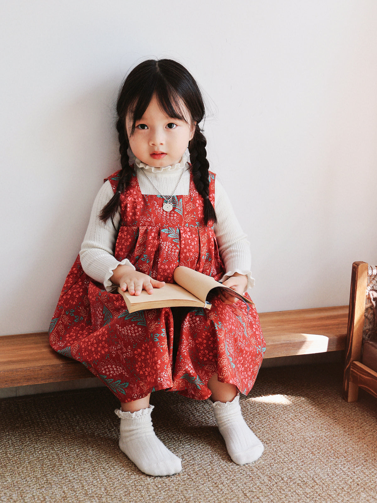 Girl wearing Holiday Bloom red floral dress with white knit layer and book