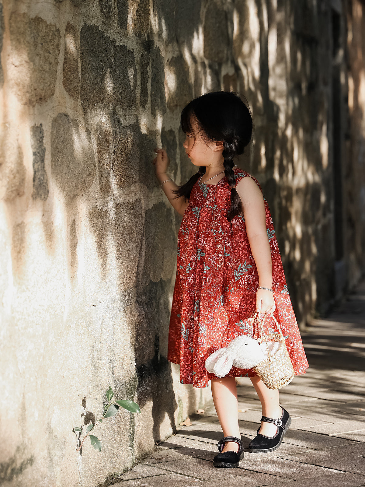 Girl wearing Holiday Bloom red floral sleeveless dress by stone wall