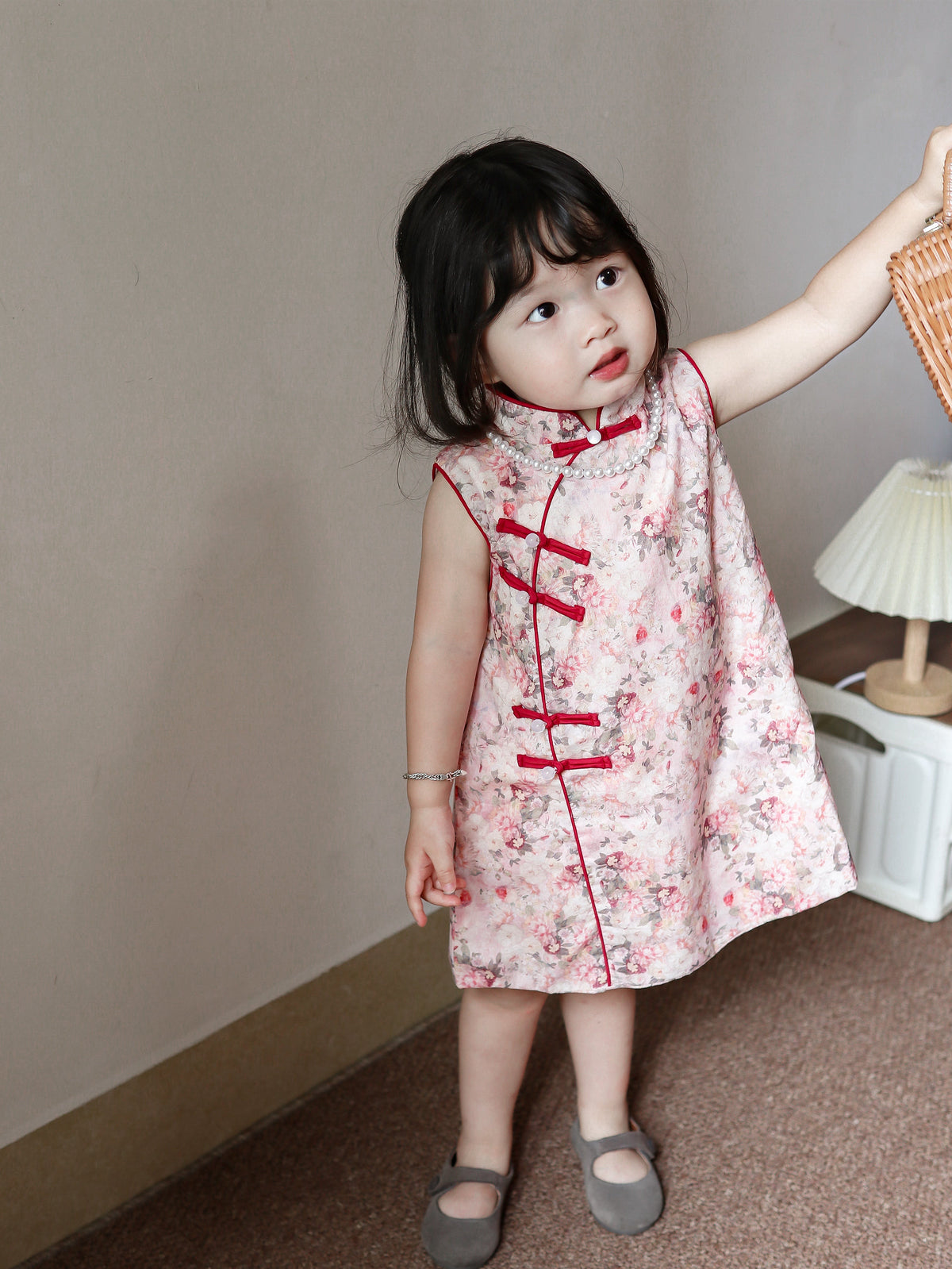 Girl wearing pink floral sleeveless qipao dress with basket in a warm home setting