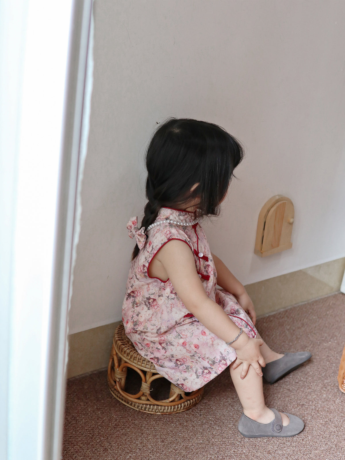 Seated back view of pink floral sleeveless qipao dress in a warm home setting