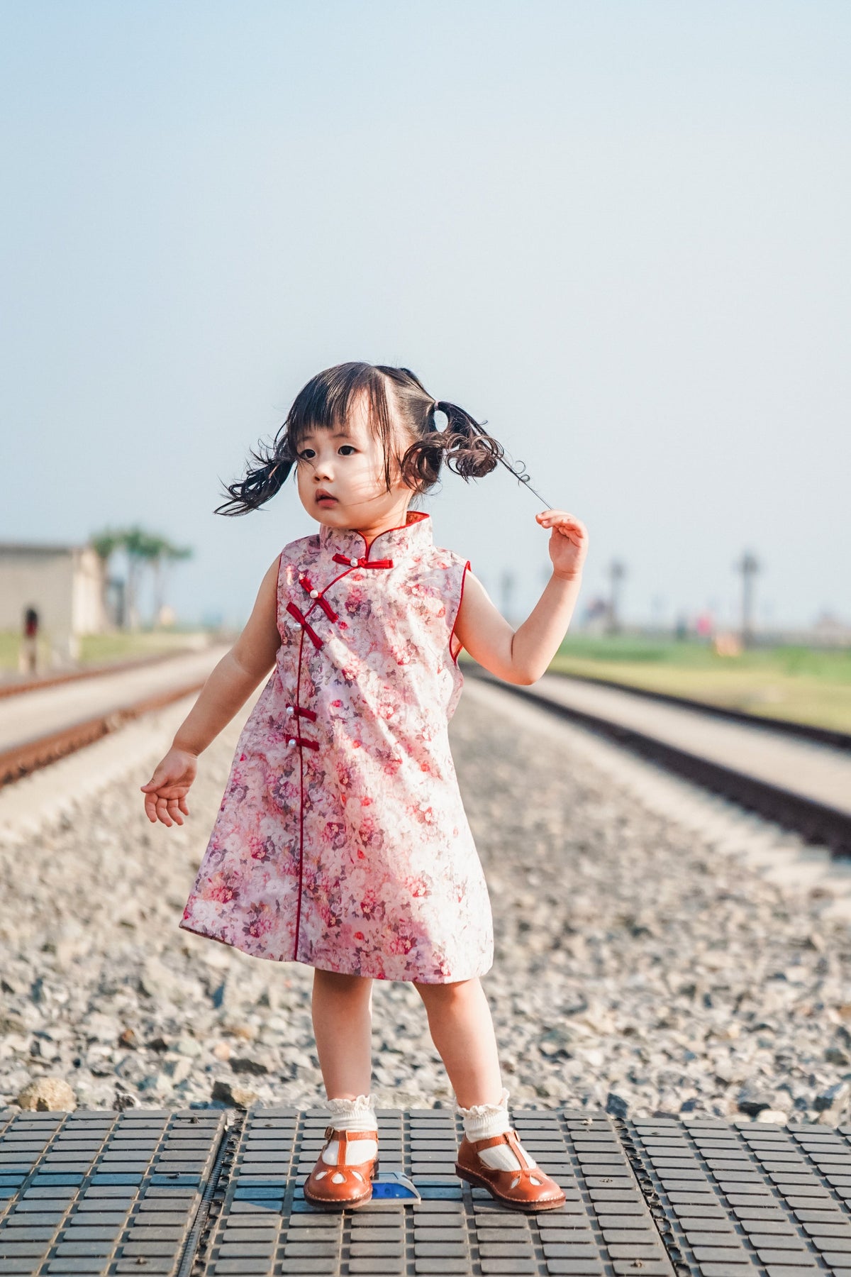 Girl wearing the pink floral sleeveless qipao dress at a railway-themed scenic attraction